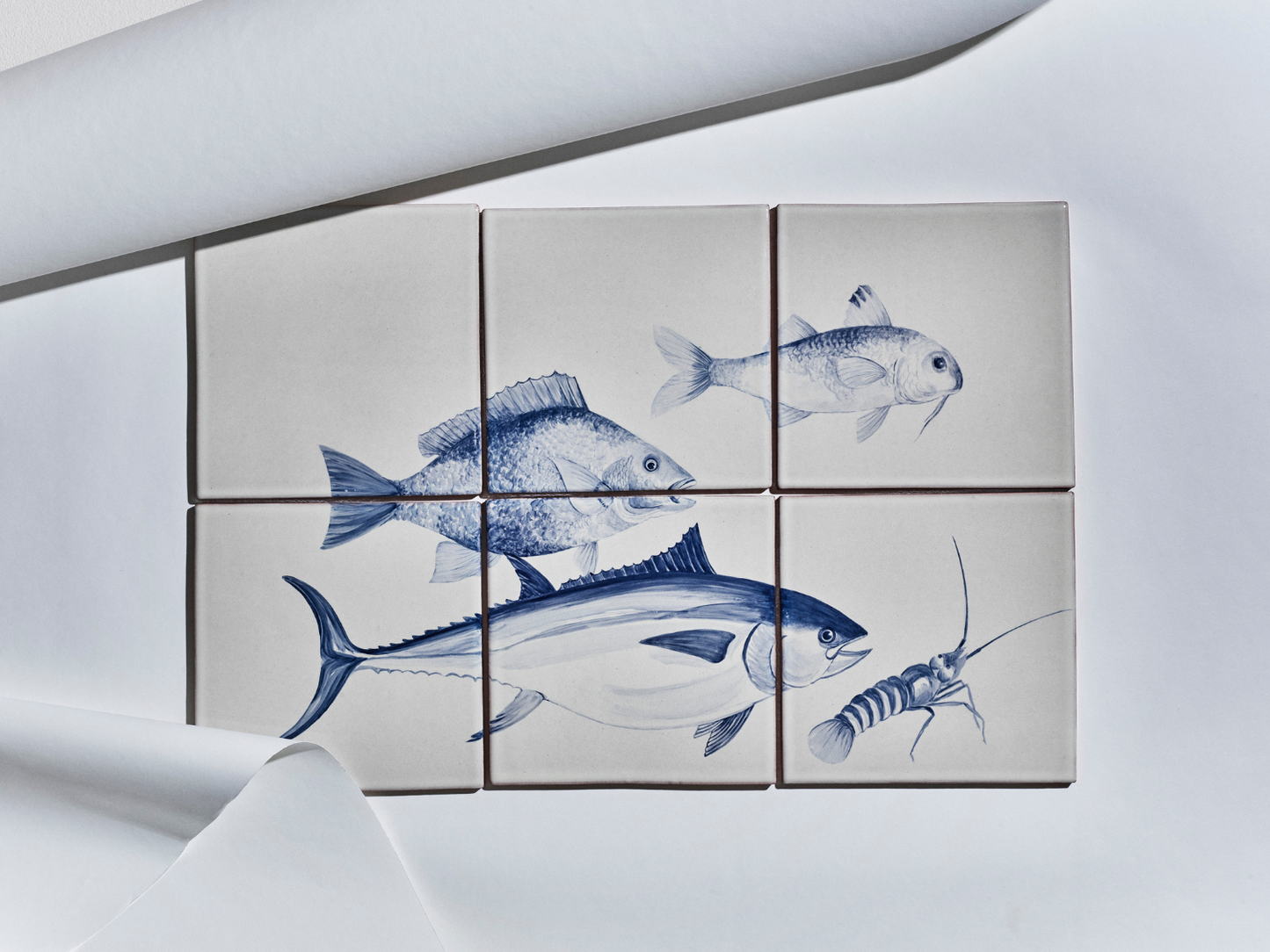 Sechsteiliges Fliesenbild mit handgemalten Meeresmotiven in Blau auf hellem Grund: Fische und ein Krebs.
Six-tile mural with hand-painted marine motifs in blue on a light background: fish and a crustacean.