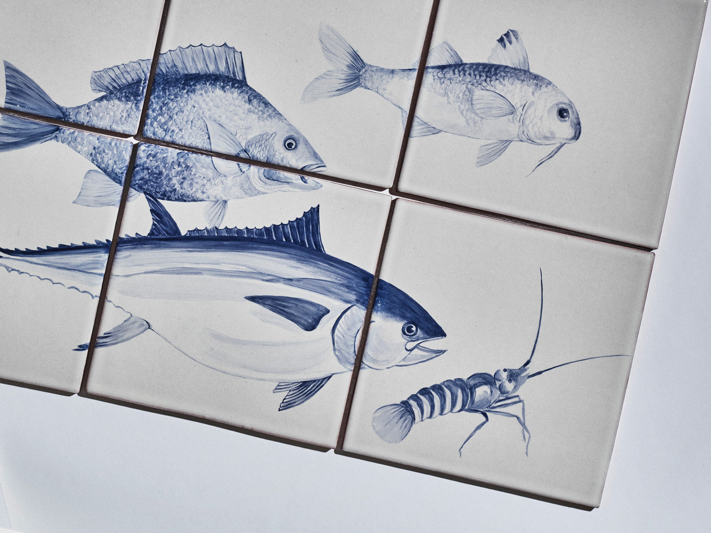 Sechsteiliges Fliesenbild mit handgemalten Meeresmotiven in Blau auf hellem Grund: Fische und ein Krebs.
Six-tile mural with hand-painted marine motifs in blue on a light background: fish and a crustacean.