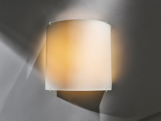 Beleuchtete Wandleuchte „Luna Pure“ aus weißem Biskuitporzellan, warm leuchtend vor grauer Wand.
Illuminated “Luna Pure” wall light made of white biscuit porcelain, glowing warmly against a grey wall.