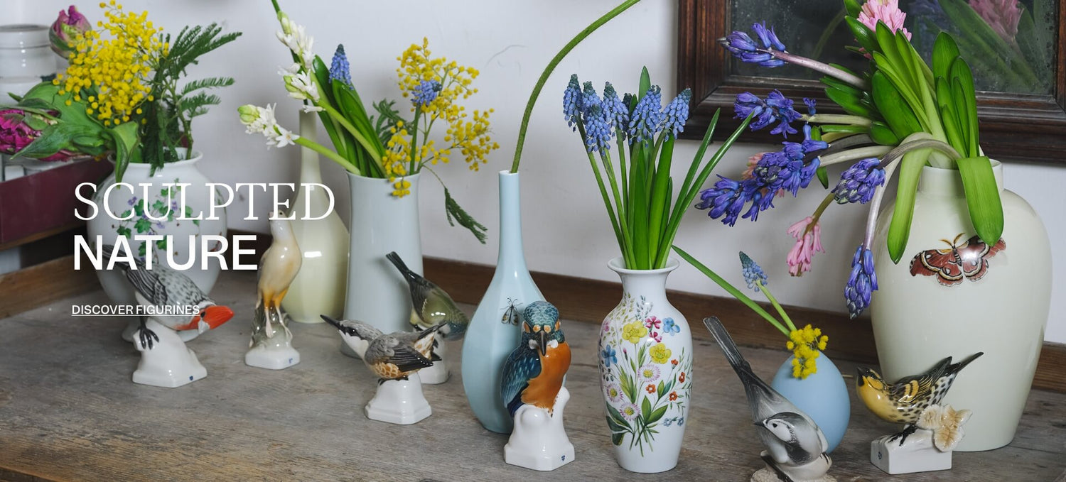 Group of white faceted porcelain cups, bowls, plates and vases arranged on a beige surface against a pale background.