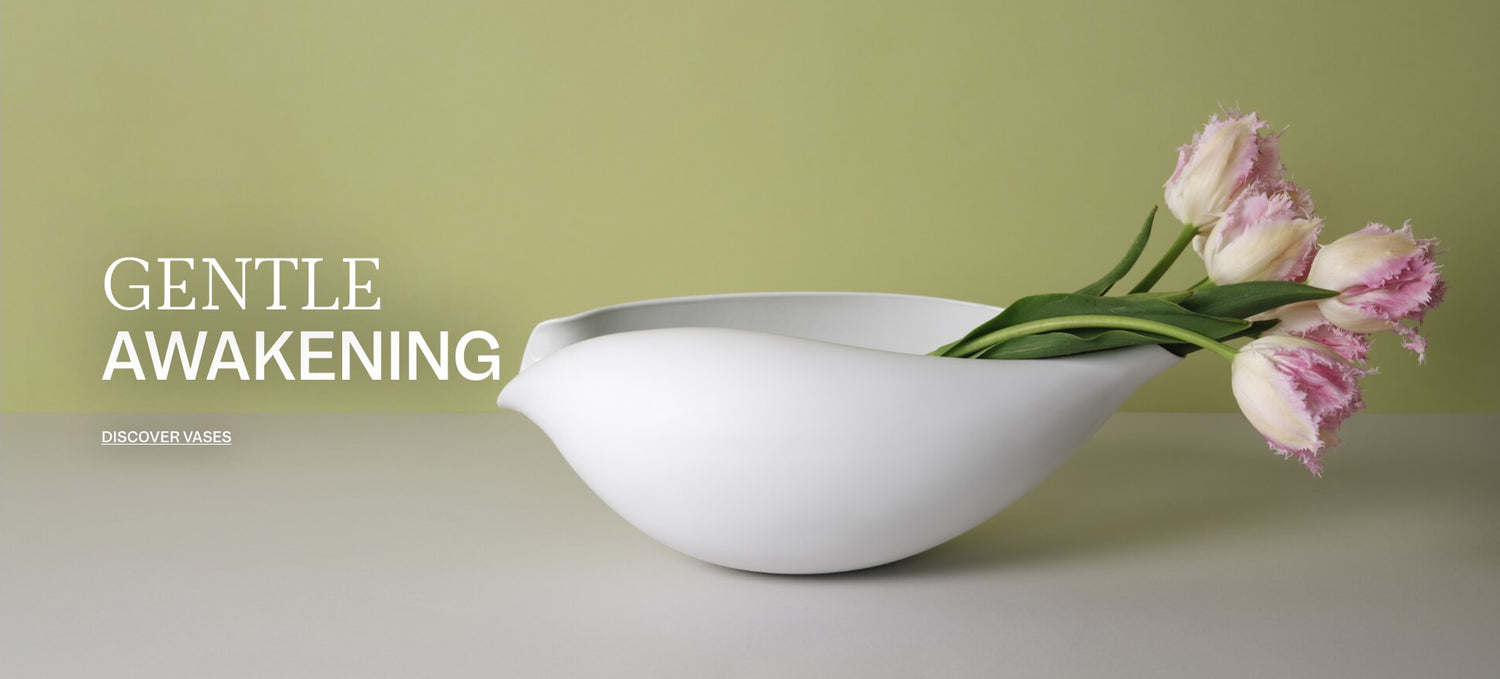 Matte white porcelain vase with pale pink fringed tulips against a soft green background; on the left, the text reads “Gentle Awakening” and “Discover Vases”.