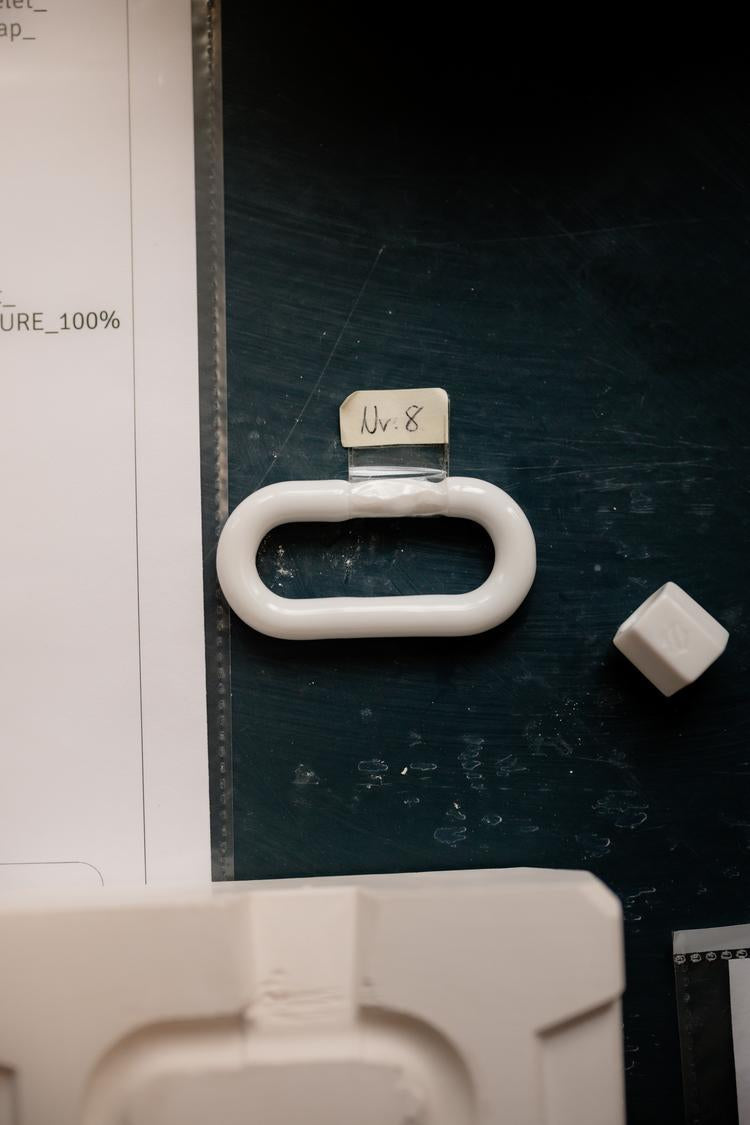 Weißes, ovales Porzellanobjekt mit der Beschriftung „Nr. 8“ liegt auf einem dunklen Tisch neben einem Papier und einem kleinen Würfelförmigen Objekt.
White, oval porcelain piece labeled “Nr. 8” lying on a dark table next to a sheet of paper and a small cube-shaped object.