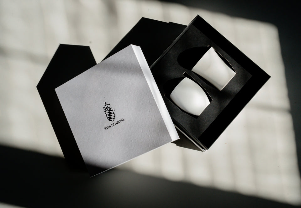 Geöffnete Nymphenburg Geschenkbox mit zwei weißen Porzellanbechern in schwarzer Einlage.

Open Nymphenburg gift box with two white porcelain cups in a black insert.