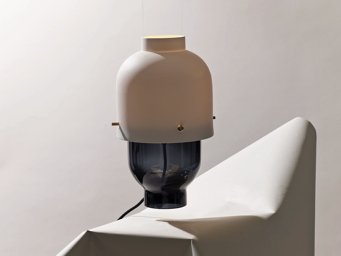 Tischleuchte „Colo“ von Nymphenburg mit mattweißem Porzellanschirm und Messingdetails auf einem rauchgrauen Glasfuß, inszeniert auf einem gefalteten Papierpodest vor neutralem Hintergrund.

Nymphenburg “Colo” table lamp with a matte white porcelain shade and brass details on a smoke-grey glass base, staged on a folded paper plinth against a neutral backdrop.