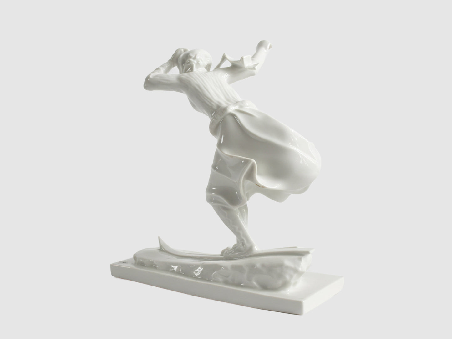 Rückansicht einer weißen Porzellanfigur einer Skifahrerin in Bewegung, mit weit schwingendem Rock auf Skiern, freigestellt vor hellem Hintergrund.

Rear view of a white porcelain figurine of a female skier in motion, with a wide swirling skirt on skis, isolated against a light background.