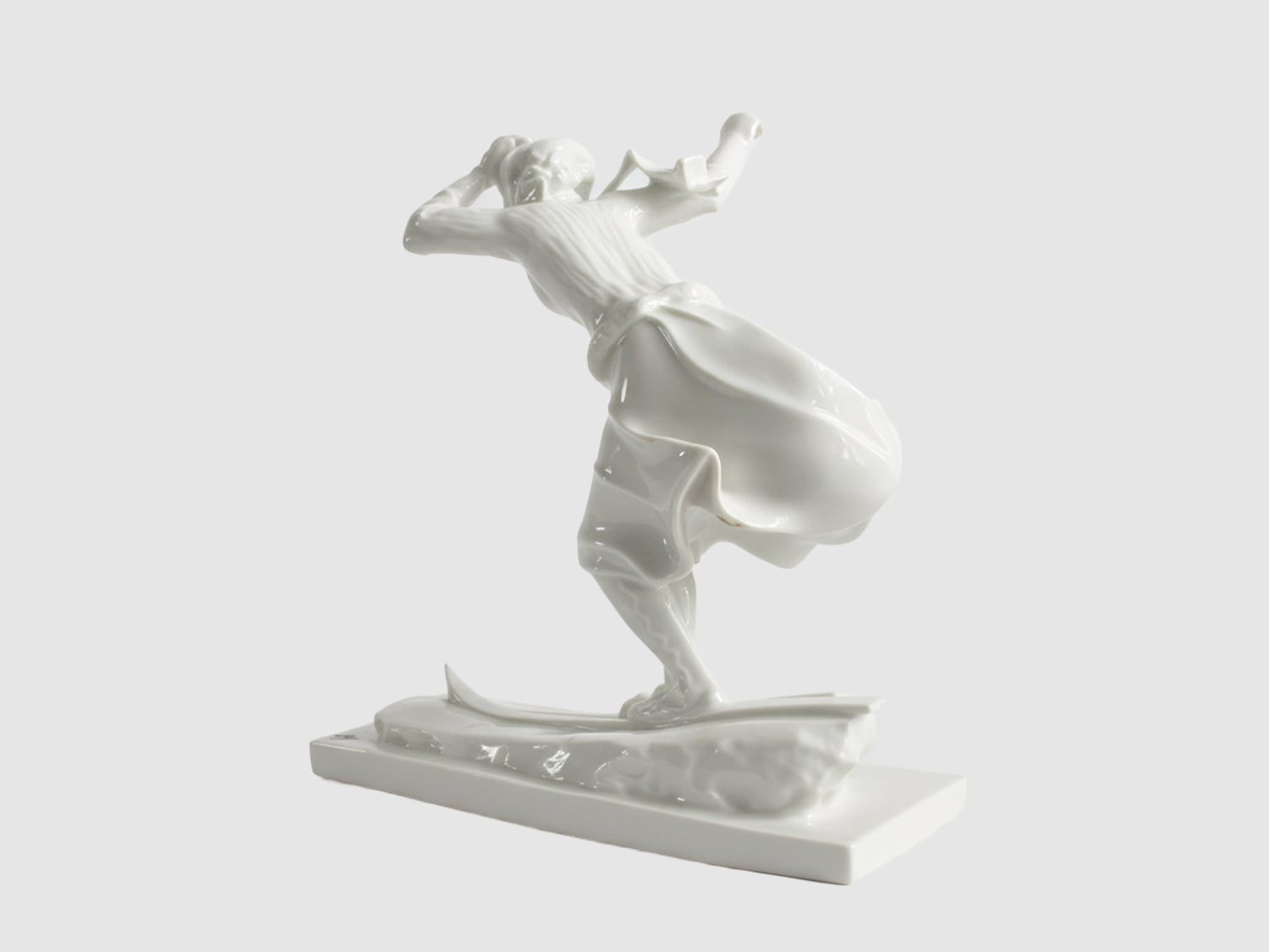 Rückansicht einer weißen Porzellanfigur einer Skifahrerin in Bewegung, mit weit schwingendem Rock auf Skiern, freigestellt vor hellem Hintergrund.

Rear view of a white porcelain figurine of a female skier in motion, with a wide swirling skirt on skis, isolated against a light background.
