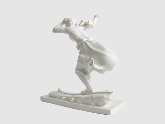 Rückansicht einer weißen Porzellanfigur einer Skifahrerin in Bewegung, mit weit schwingendem Rock auf Skiern, freigestellt vor hellem Hintergrund.

Rear view of a white porcelain figurine of a female skier in motion, with a wide swirling skirt on skis, isolated against a light background.