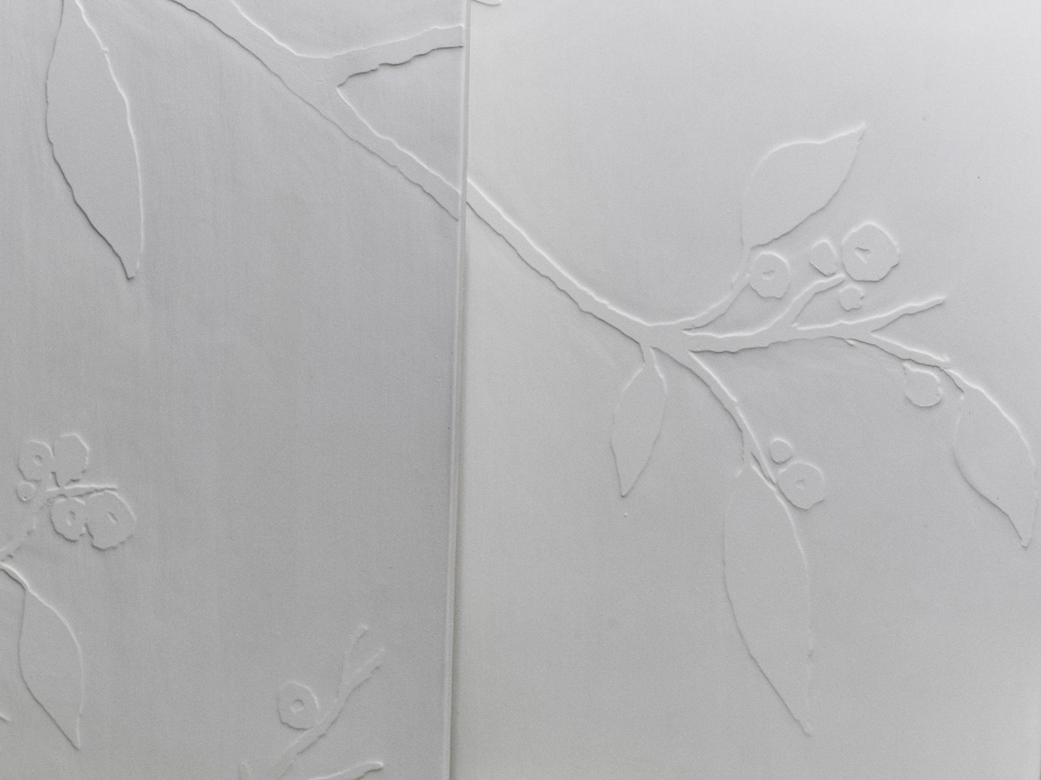 Nahaufnahme zweier Kirschblüten-Fliesen mit ineinanderlaufendem Astrelief.

Close-up of two cherry blossom tiles with an interlocking branch relief.